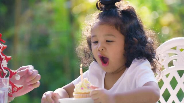 Happy Asian family birthday party. Close up of Adorable child girl blows out candle on small birthday cake with smile face. Happy little cute daughter celebrate birthday with father and mother at home