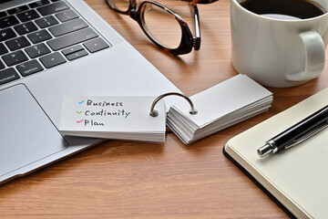 There's a laptop computer, a notebook, a pen and an open vocabulary book on the desk. The word Business Continuity Plan is written on it.