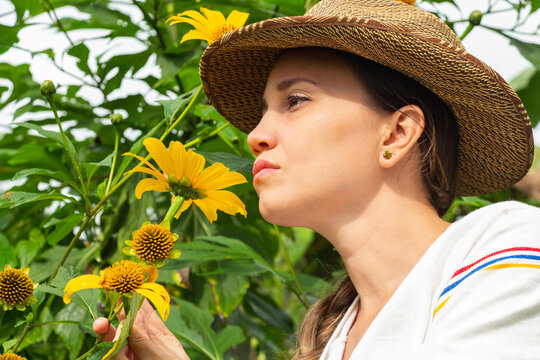 Hermosa mujer con sombrero oliendo flores silvestres amarillas en el campo