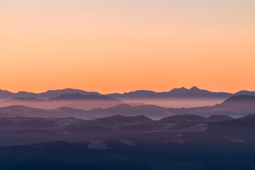 High mountain ranges in dense fog. Layers of mountains in the haze during sunset. Multi-layered foggy mountains.