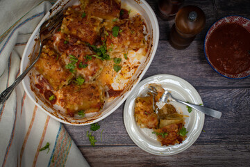Vegetarian lasagna rolls filled with seitan in white dish on wooden table