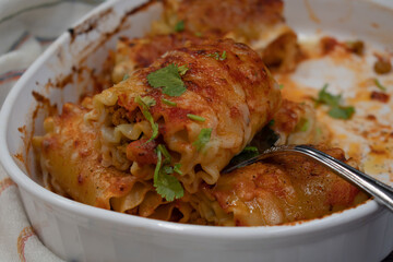 Vegetarian lasagna rolls filled with seitan in white dish on wooden .table, close up