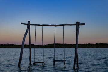 solitary swings in the middle of the sea at sunset