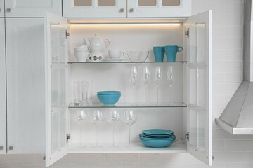 Fototapeta na wymiar Open cabinet with different clean dishware in kitchen