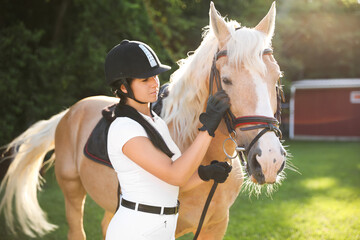 Young woman in horse riding suit and her beautiful pet outdoors on sunny day