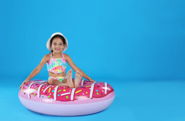 Cute little child in beachwear with inflatable ring on light blue background. Space for text