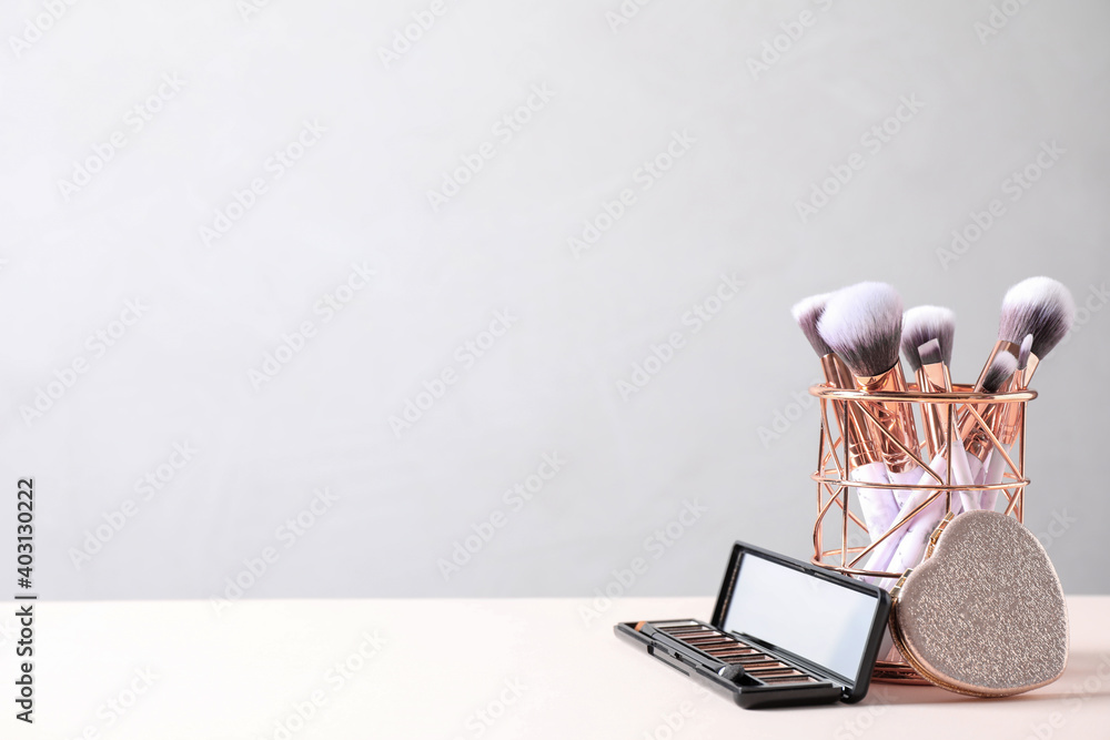 Wall mural Make up brushes in holder and cosmetic products on white table. Space for text