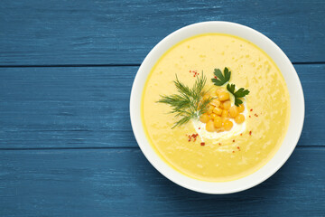 Delicious creamy corn soup served on blue wooden table, top view. Space for text