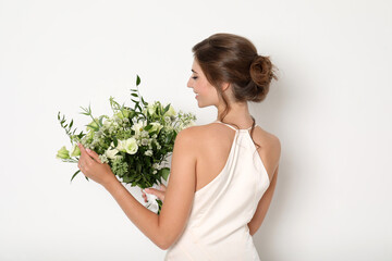 Young bride wearing wedding dress with beautiful bouquet on light background
