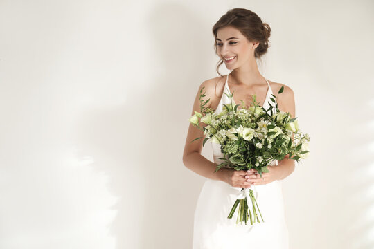 Young bride wearing wedding dress with beautiful bouquet on light background. Space for text
