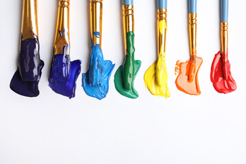 Set of brushes with different paints on white background, flat lay. Rainbow colors