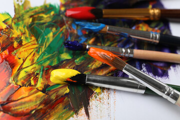 Set of brushes with different paints on artwork, closeup