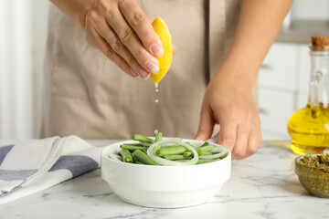 Woman adding lemon juice to green beans at white marble table, closeup