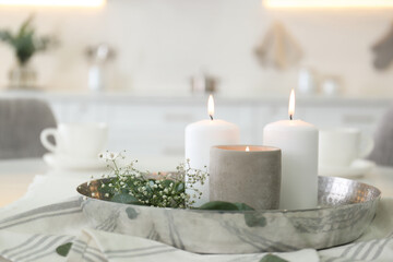 Beautiful eucalyptus branches, flowers and burning candles on napkin in kitchen. Interior element