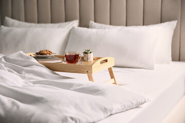 Wooden tray with breakfast and book near soft blanket on bed