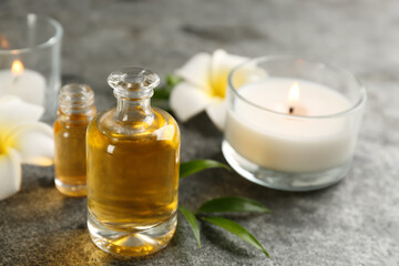 Beautiful spa composition with essential oil, candles and flowers on grey table, closeup