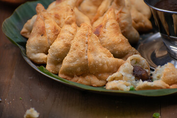Traditional potato masala samosas and tamarind chutney on platter with banana leaf