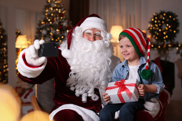 Fototapeta na wymiar Santa Claus and little boy taking selfie in room decorated for Christmas