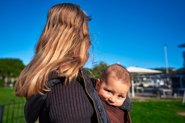 Young mother with baby in sling in the park on sunny autumn day