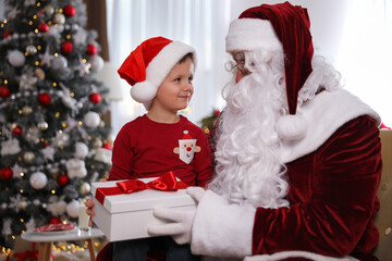 Fototapeta na wymiar Santa Claus giving present to little boy in room decorated for Christmas