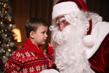 Fototapeta na wymiar Little boy whispering in Santa Claus' ear near Christmas tree indoors