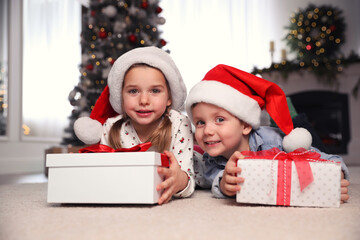 Fototapeta na wymiar Cute little children with Christmas gifts on floor at home
