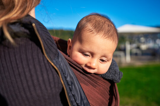 Young mother with baby in sling in the park on sunny autumn day