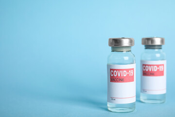 Vials with coronavirus vaccine on light blue background, space for text