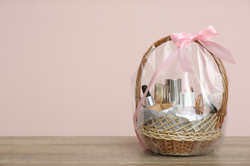 Wicker gift basket with cosmetic products on wooden table. Space for text