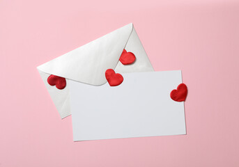 Blank card, envelope and red decorative hearts on pink background, flat lay with space for text. Valentine's Day celebration