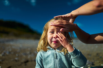 Preschooler on the beach is having suncream applied