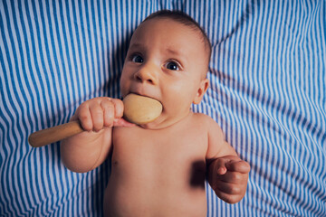 Baby on bed with wooden rattle