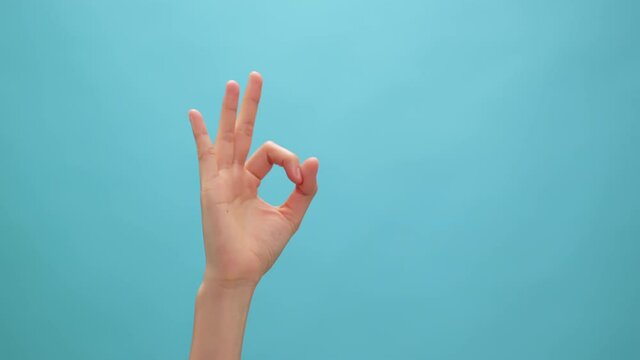 Close up of woman hand showing ok sign okay gesture on the blue background.