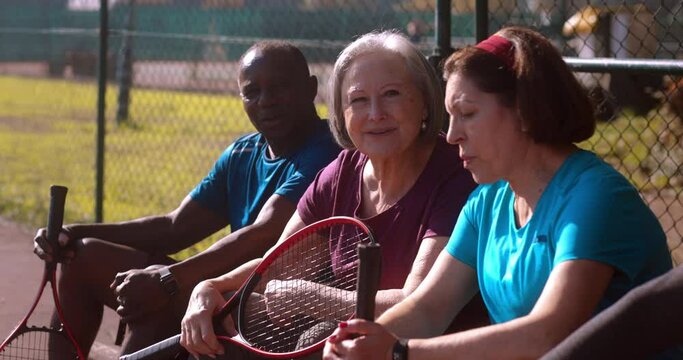 Group of seniors resting after tennis game on bech