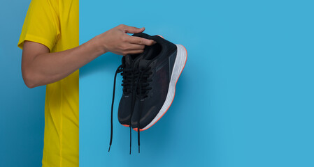 Male hand holding running shoes on blue background,copy space for text