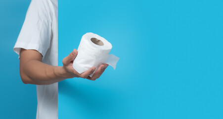 Male hand holding white toilet paper roll on blue background,copy space for text