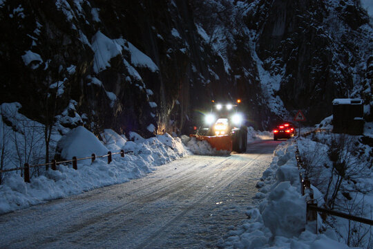 snowplow passes through the snowy mountain streets in the evening to clean up the road traffic