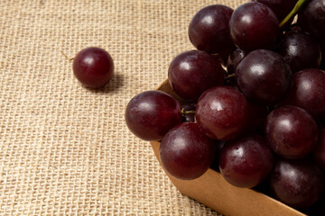 Bunch of red grapes in rustic paper box, on jute fabric
