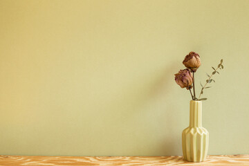 Vase of dry rose flowers on wooden table. khaki background