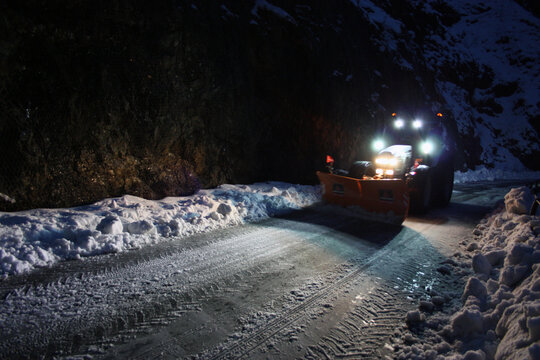 snowplow passes through the snowy mountain streets in the evening to clean up the road traffic