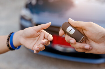 Close up woman holding new car systems key of blue hatchback car after buying from dealer at outdoor.