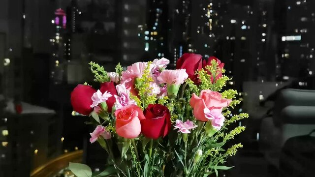 rotation of bouquet of red pink rose and carnation flowers with green leaves with blurred view of city night lights. romantic concept for lovers and valentine