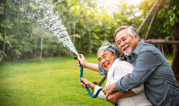 Elderly Couple Asian Happy Using A Hose To Spray Water On The Plants