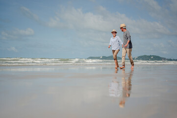 Senior couple running on the beach at sunny day. Plan life insurance with the concept of happy...