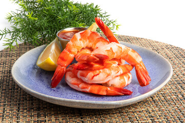 a pile of cooked, peeled and de-veined cocktail shrimp on a blue plate with cocktail sauce
