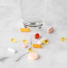 Vitamins and supplements scattered on a table with a glass of water in behind.