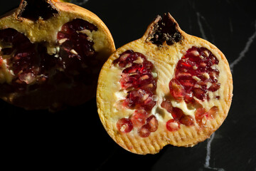 Fresh pomegranate fruit sliced in two pieces with a low ley light on a black marble surface with upper negative space.