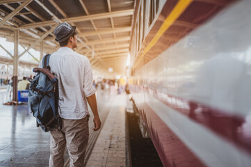 Asian man traveler with backpack in the railway, Backpack  and wearing hat at the train station with a traveler. Travel concept. Man traveler tourist walking at train station.