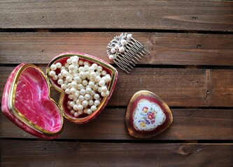 Valentine Day card concept. Shabby Chic wedding invitation concept. Pearls, pink heart jewelry box, silver hair accessory, antique keepsake box with flowers on brown wooden background. 