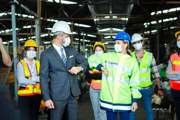 Female industrial engineer worker and foreman with face mask greeting by bumping elbows instead, keep social distance, prevent covid-19 virus infection spread at manufacturing plant factory